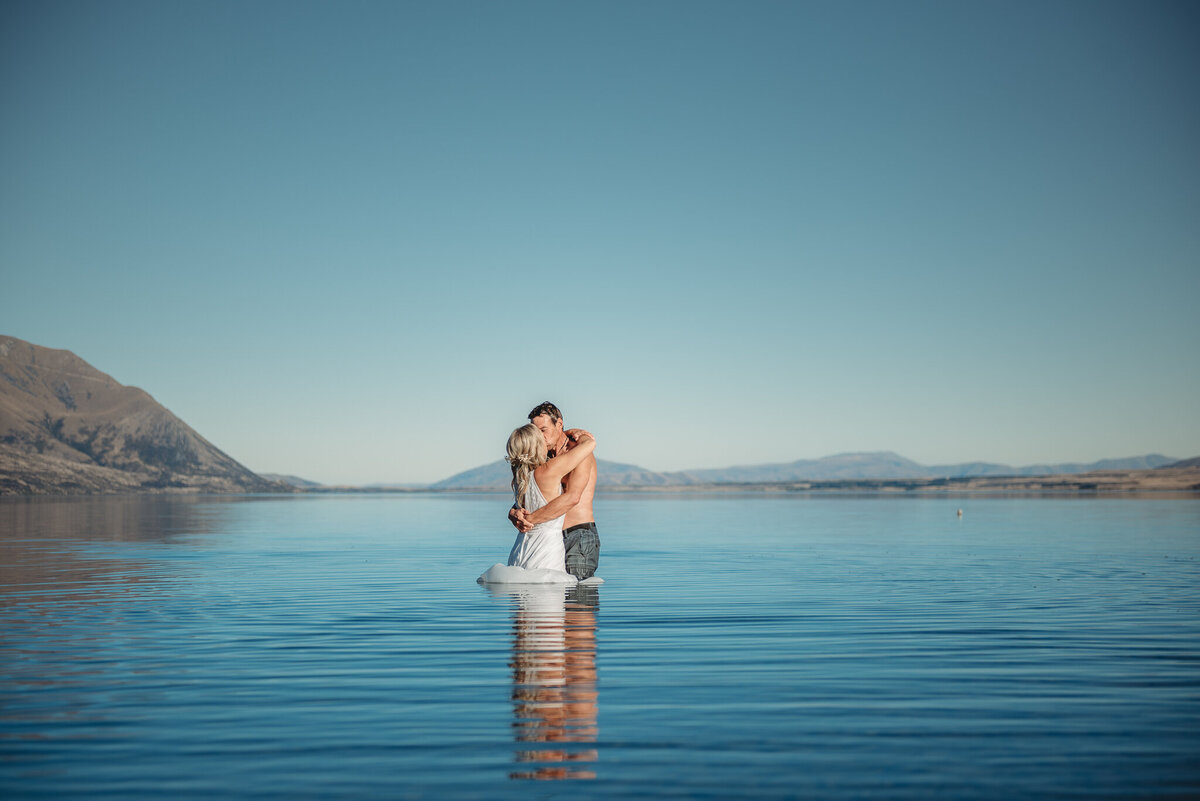 Sunset elopement in Lake Wanaka. Couple in wedding attire standing in Lake Wanaka.
