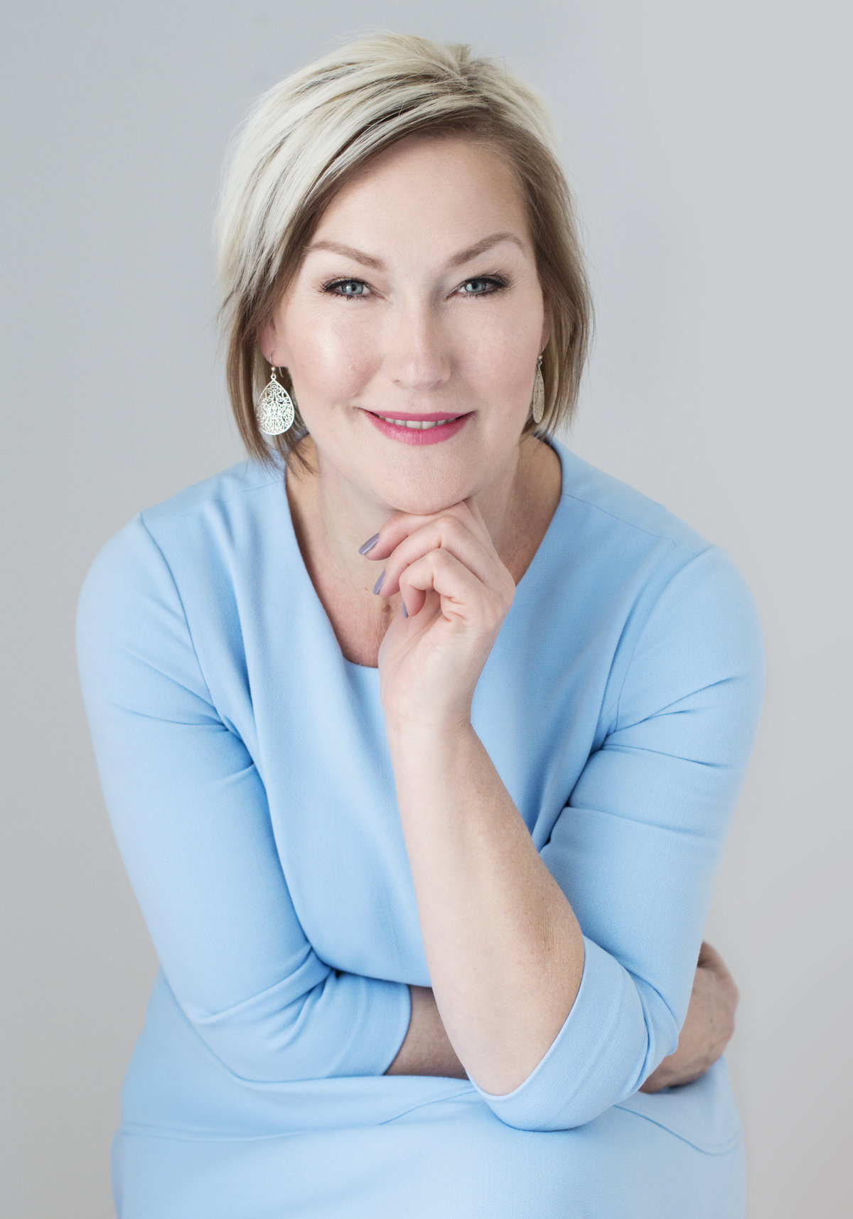 head shot  of  woman in business very confident and  leader wearing aqua blue top with  short hair smiling with her hand  under her chin