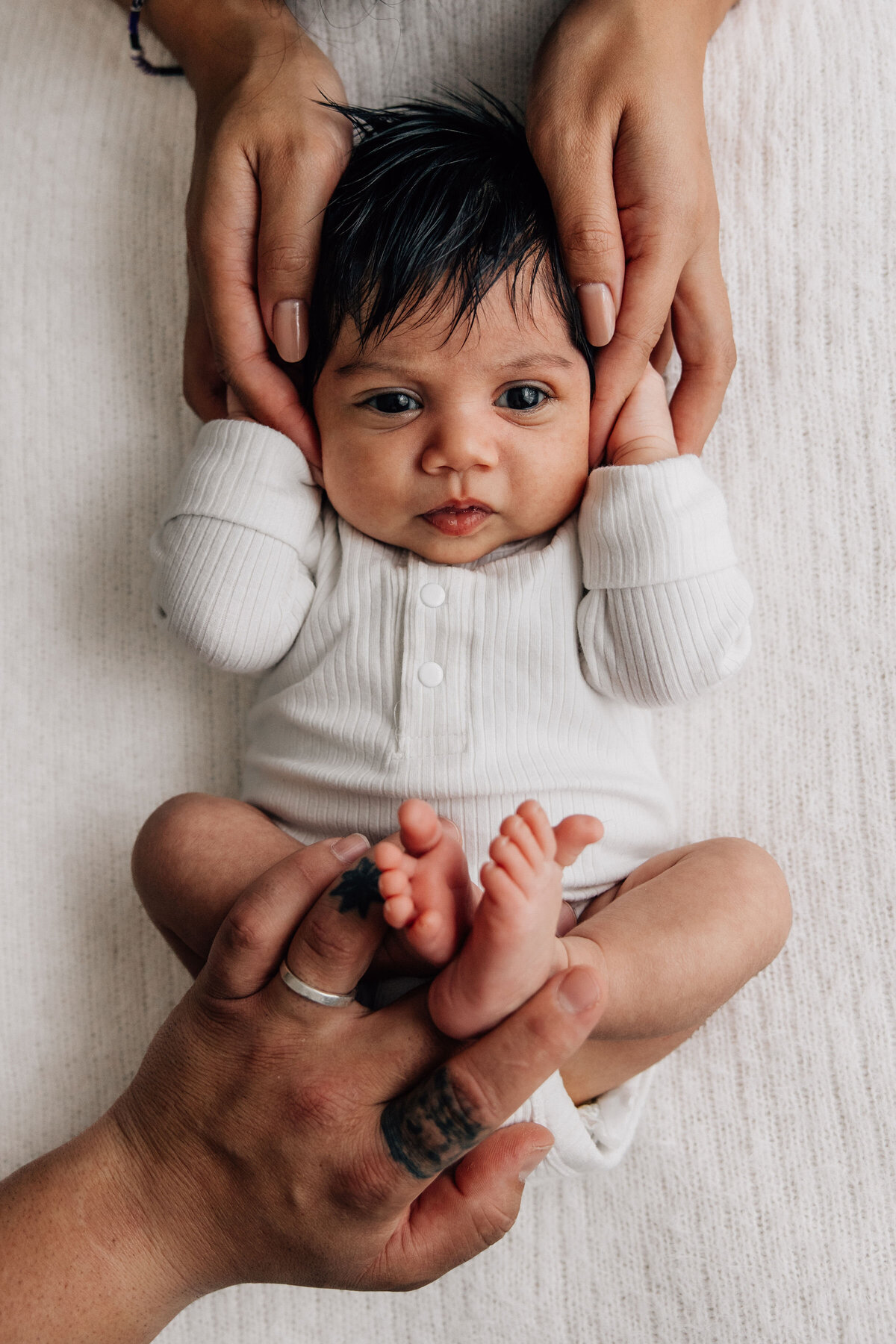 Newborn baby held by hands and feet looks at camera