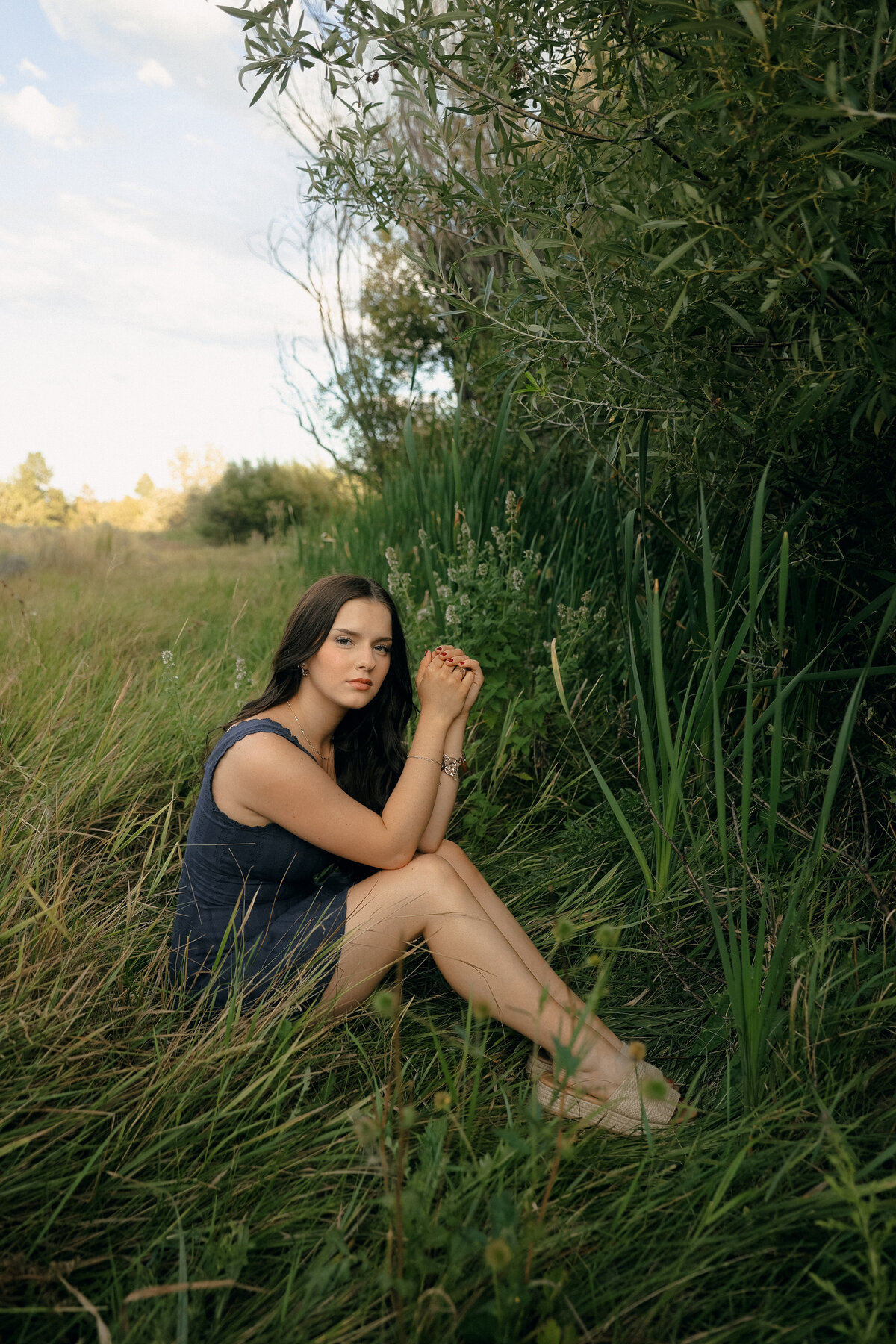 Editorial Graduation Portrait of Senior in Cap and Gown on Grassy Field Under Blue Sky