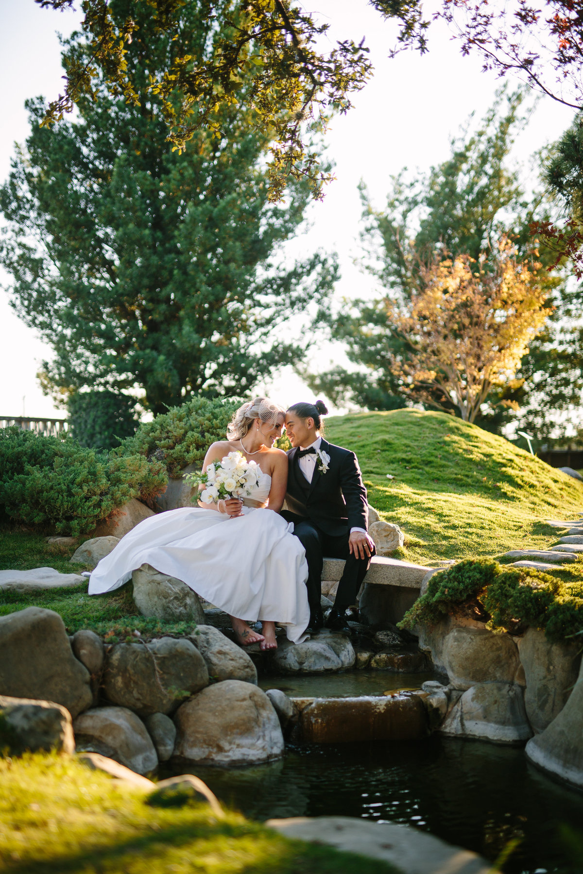 Bride and groom taking a moment after their wedding ceremony at the San Antonio Botanical Garden. They sitting atop a small waterfall and the bride is not wearing any shoes.