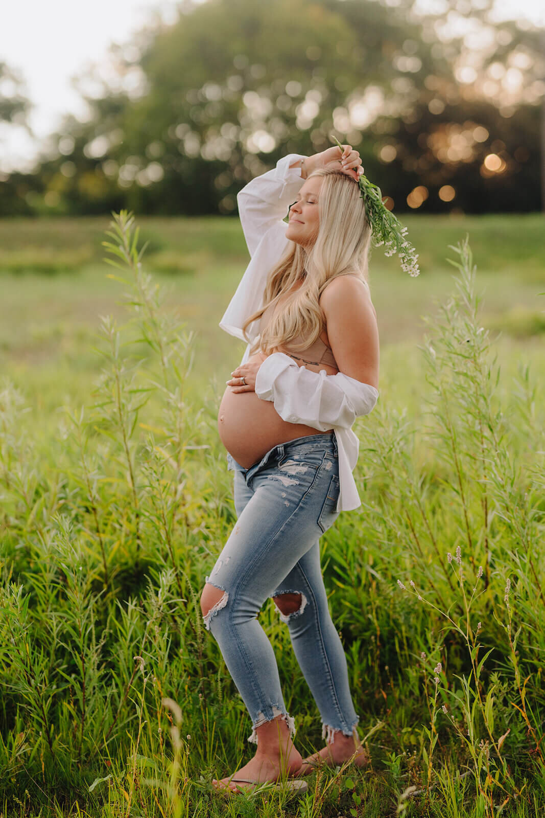 woman holding baby bump and bouquet of flowersstanding in a field