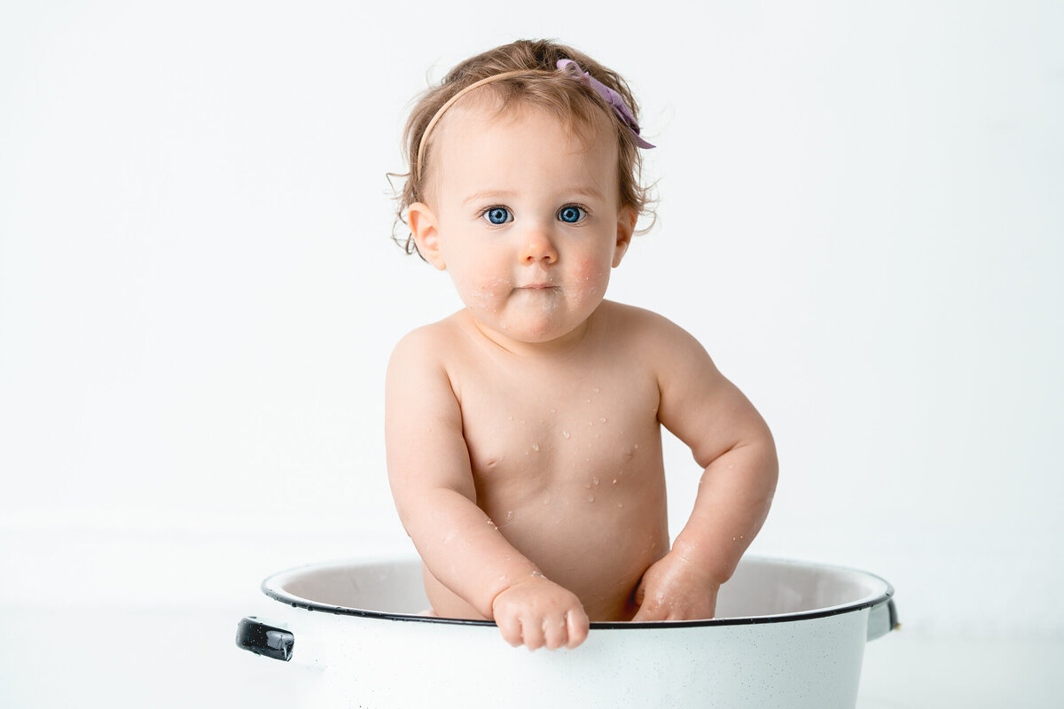 Baby girl sits in a white tub after her cake smash session at Ashley Zohil Photography Studio.
