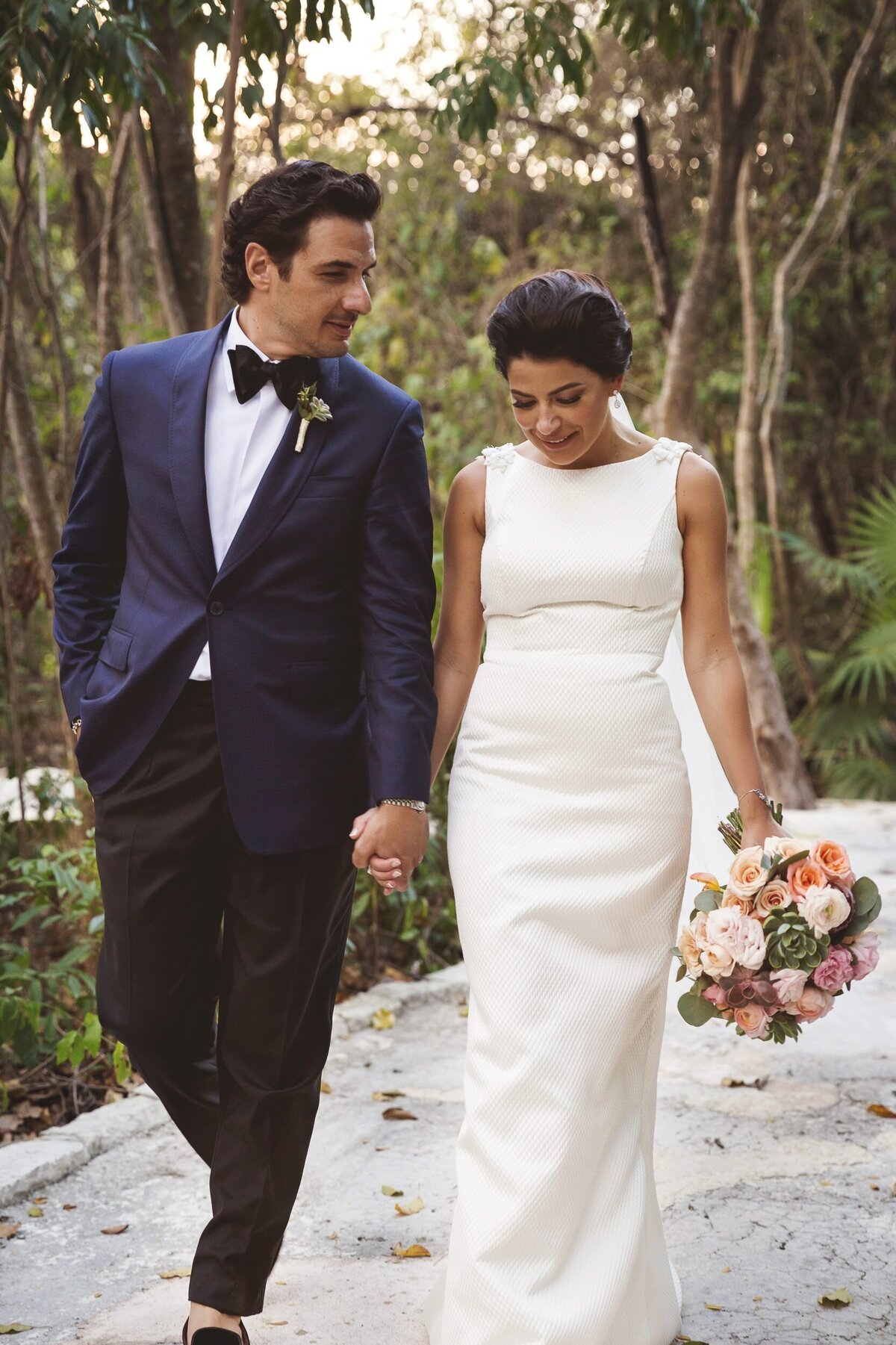 Bride and groom holding hands walking on path atBanyan Tree Riviera Maya