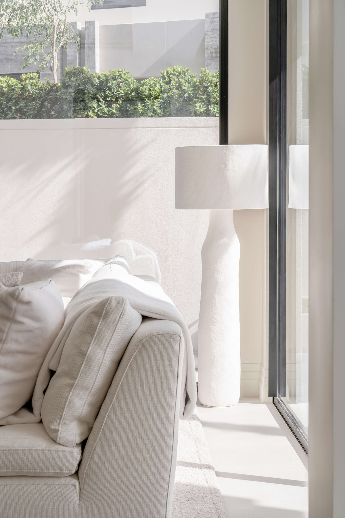 Large floor-to-ceiling windows in a bright, airy living room featuring a white couch atop a light, textured rug.