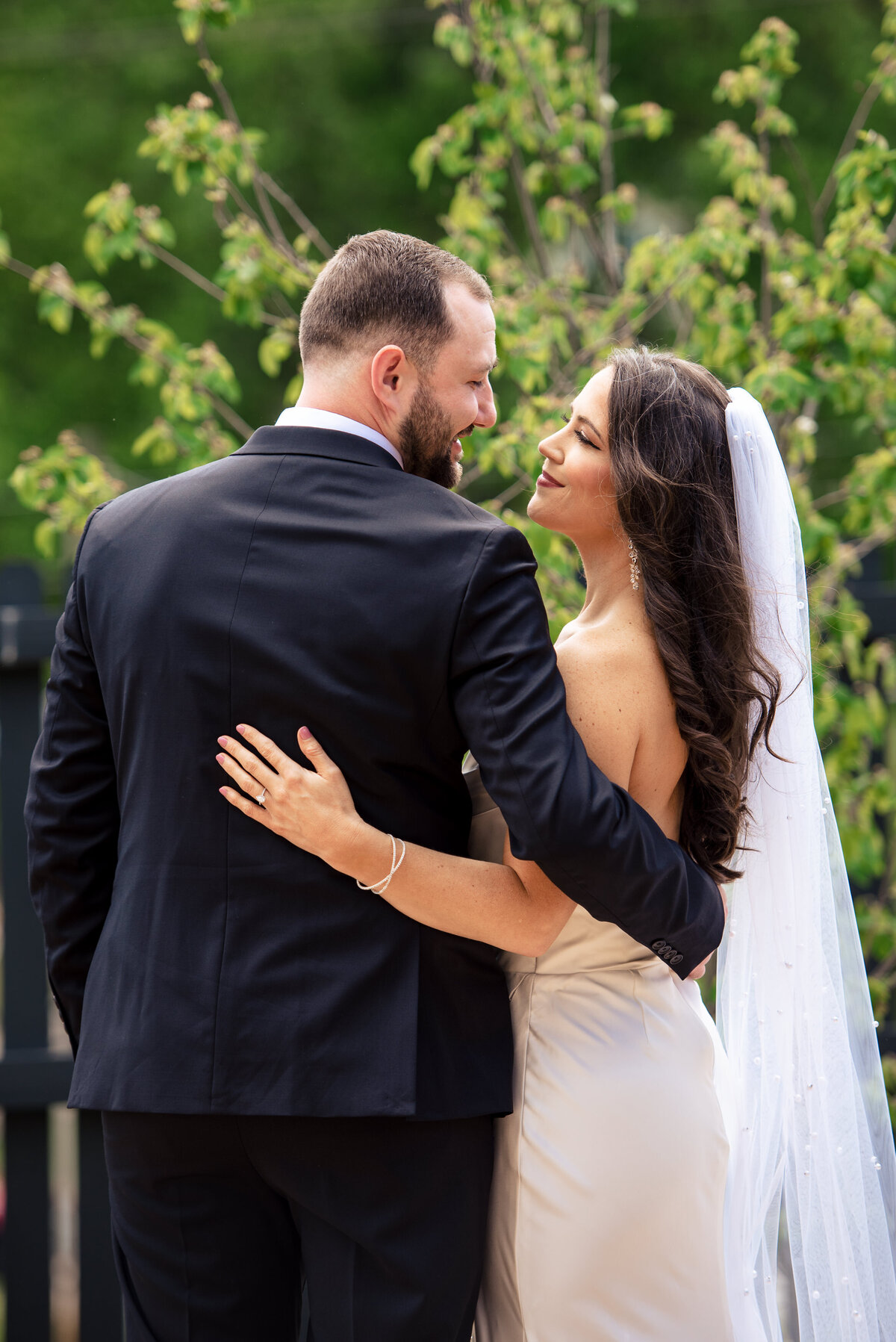 Portrait of bride and groom looking into each other's eyes and smiling with their arms around each other with their backs to the camera amid greenery outside Upstairs Atlanta by Charlotte wedding photographers DeLong Photography