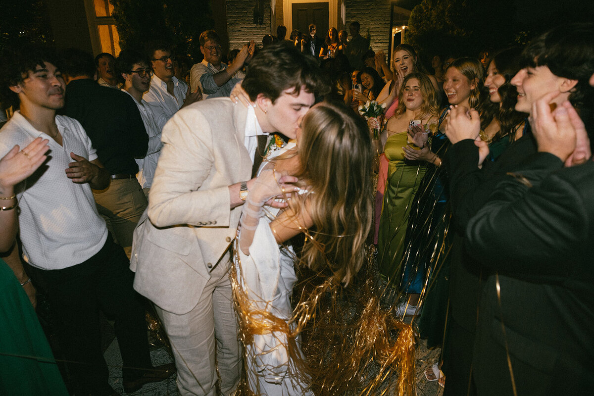 Bride and groom kiss under streamers during nighttime reception exit.