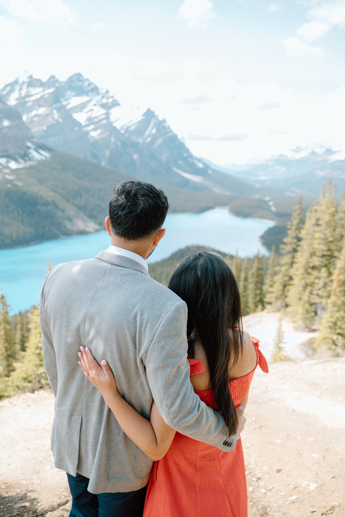 Newly engaged couple embracing each other while looking out at Peyto lake during an engagement session.