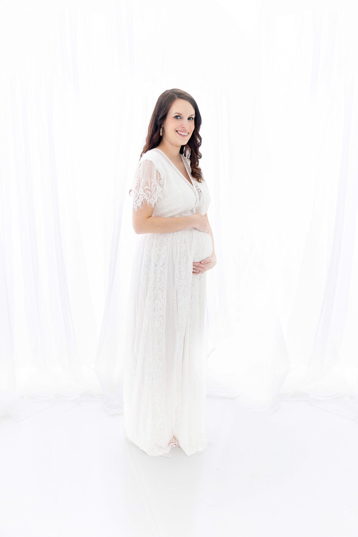 pregnant mother holding her belly in a white dress smiling at the camera