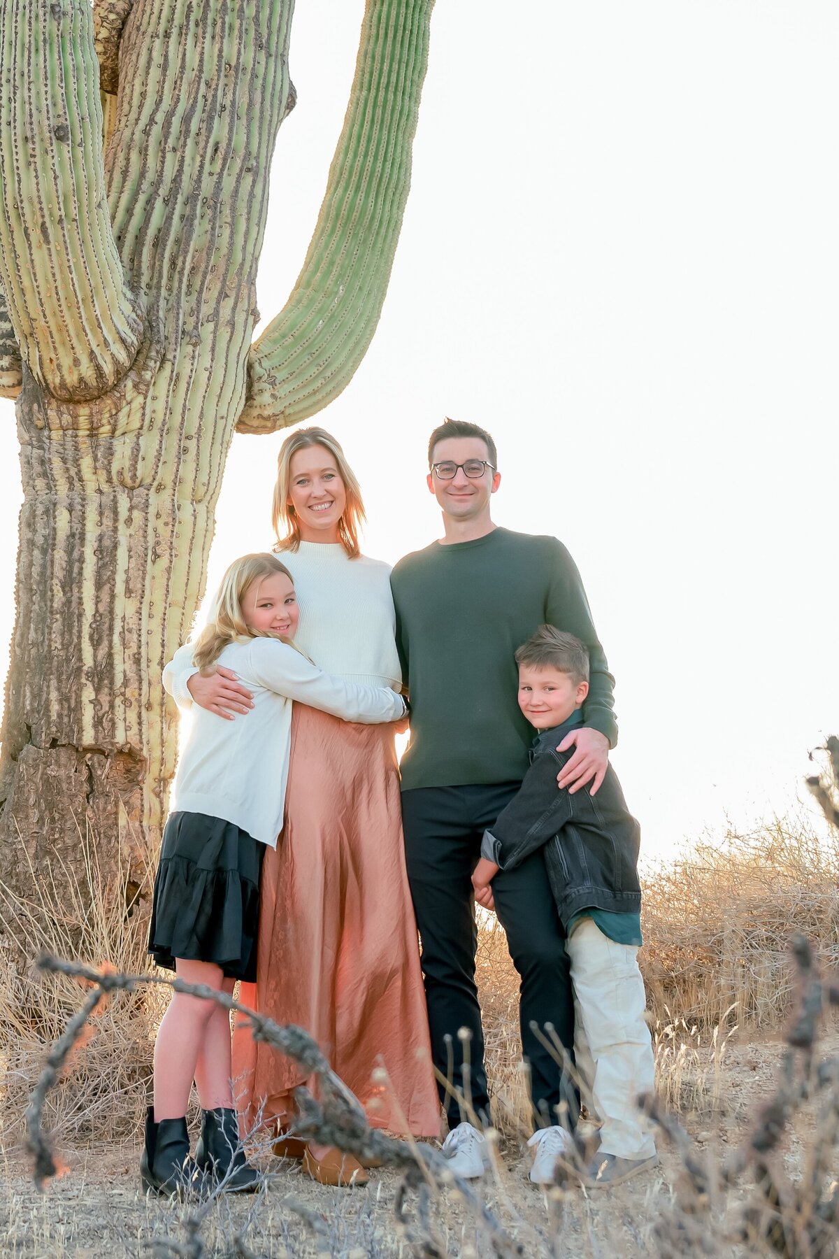 family of 4 smailing at the camera under a cactus