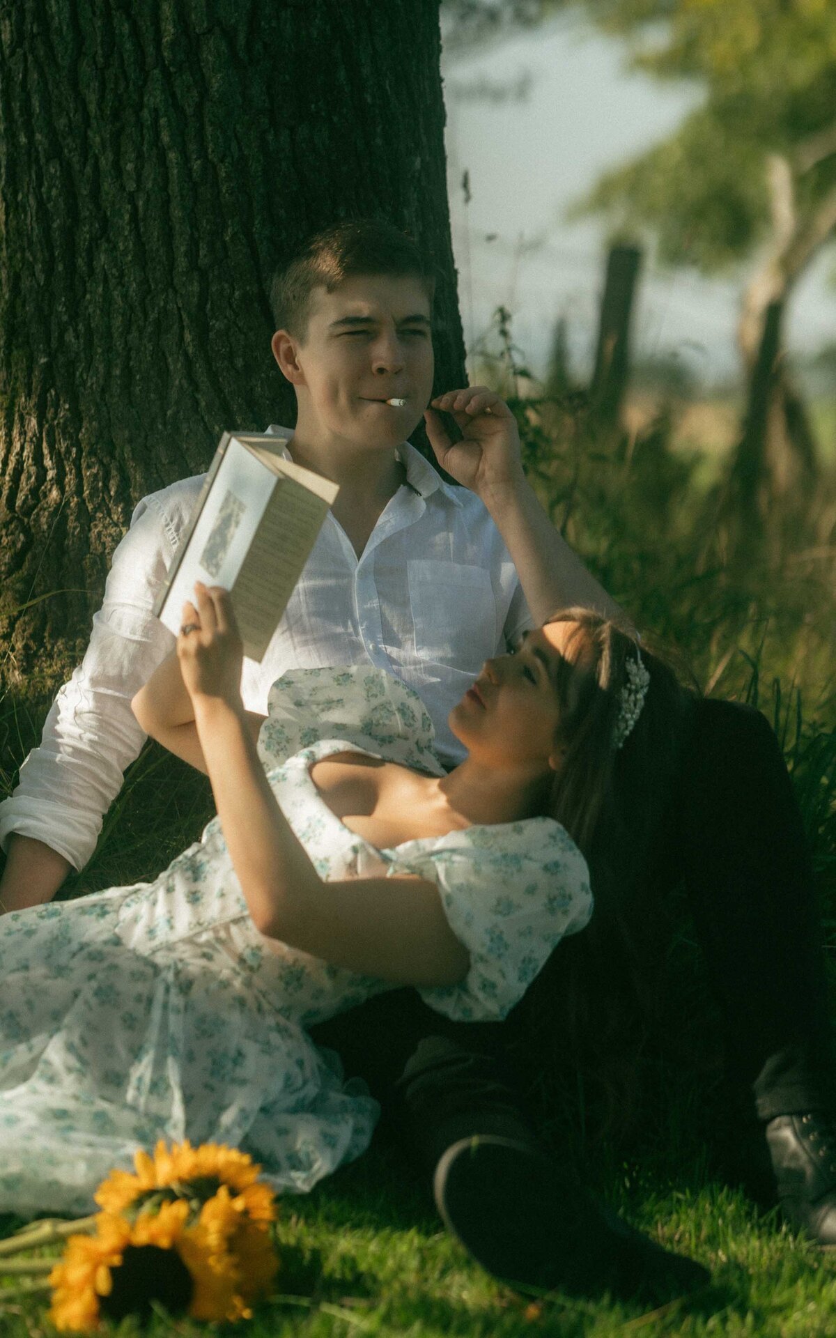 Capture a serene and relaxed couple photoshoot next to a tree. This peaceful outdoor setting reflects the couple's intimate connection, with the natural surroundings enhancing their effortless bond