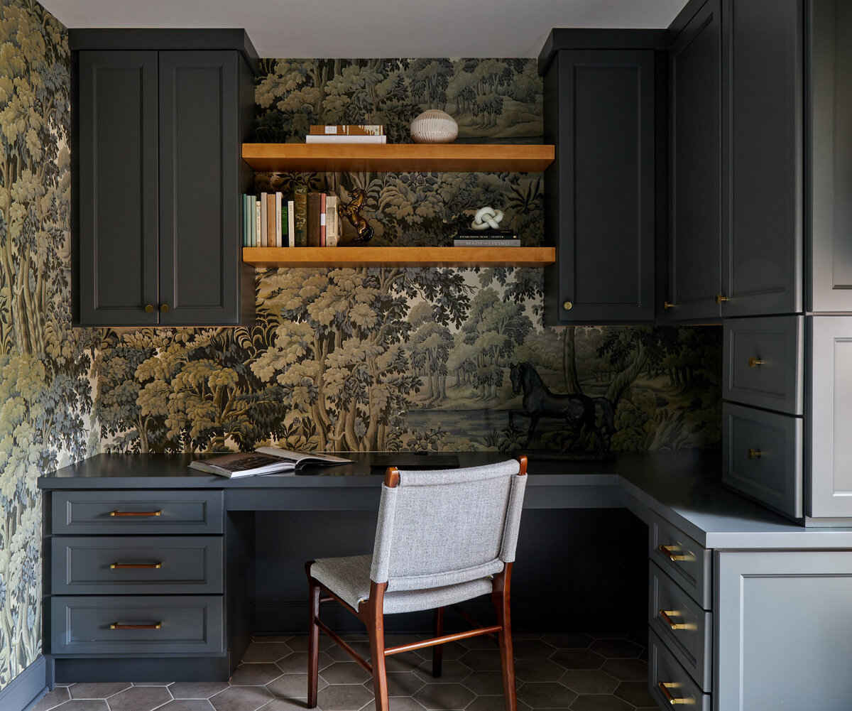 Office nook with ornate wallpaper and blue cabinets with office chair