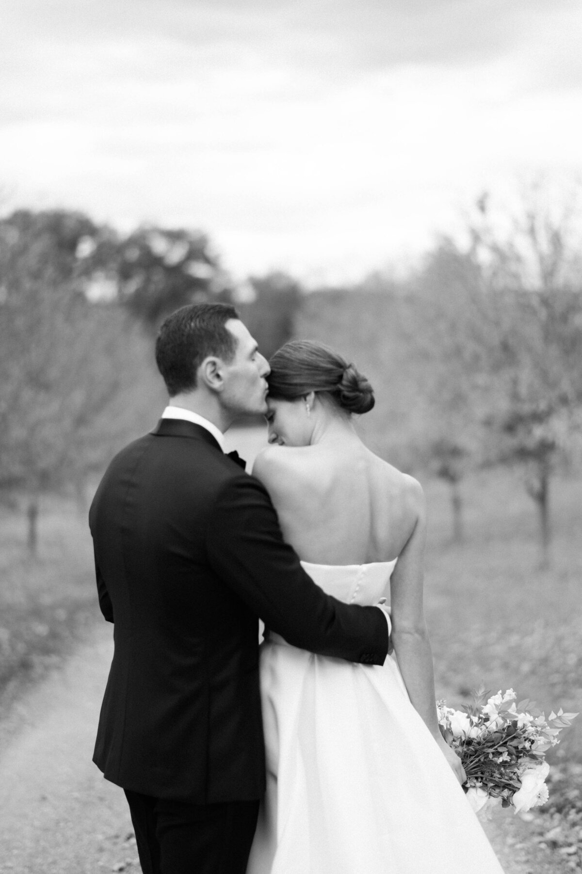 The groom kisses the bride’s head as she leans into him, eyes closed