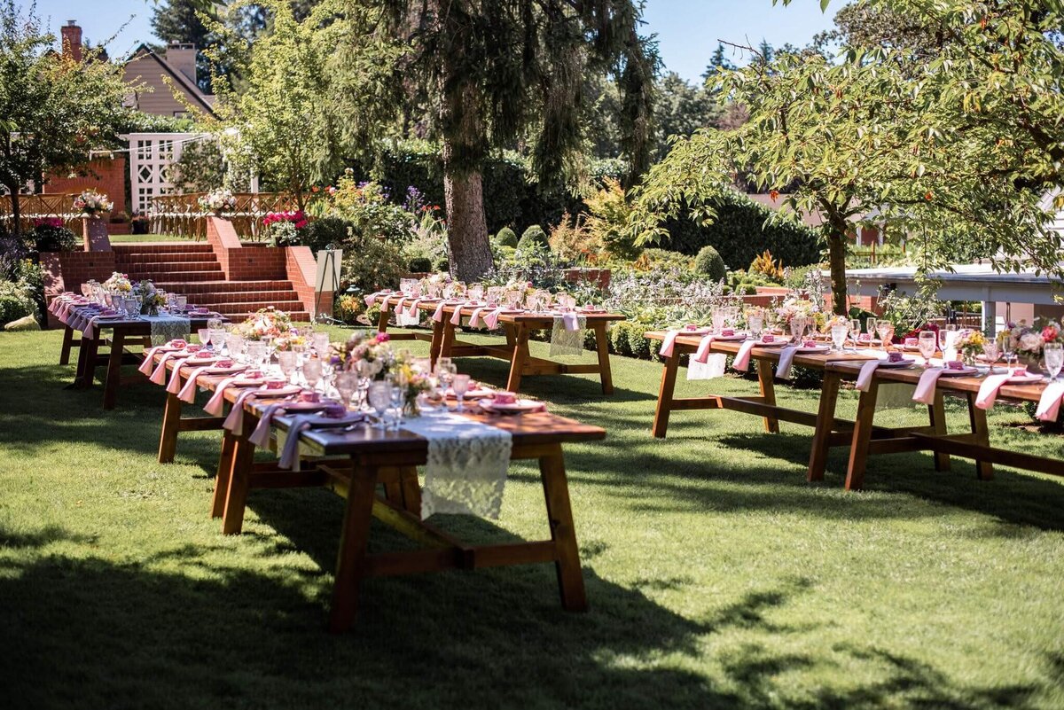 Tables with place settings and large floral arrangements at a Summer garden wedding.