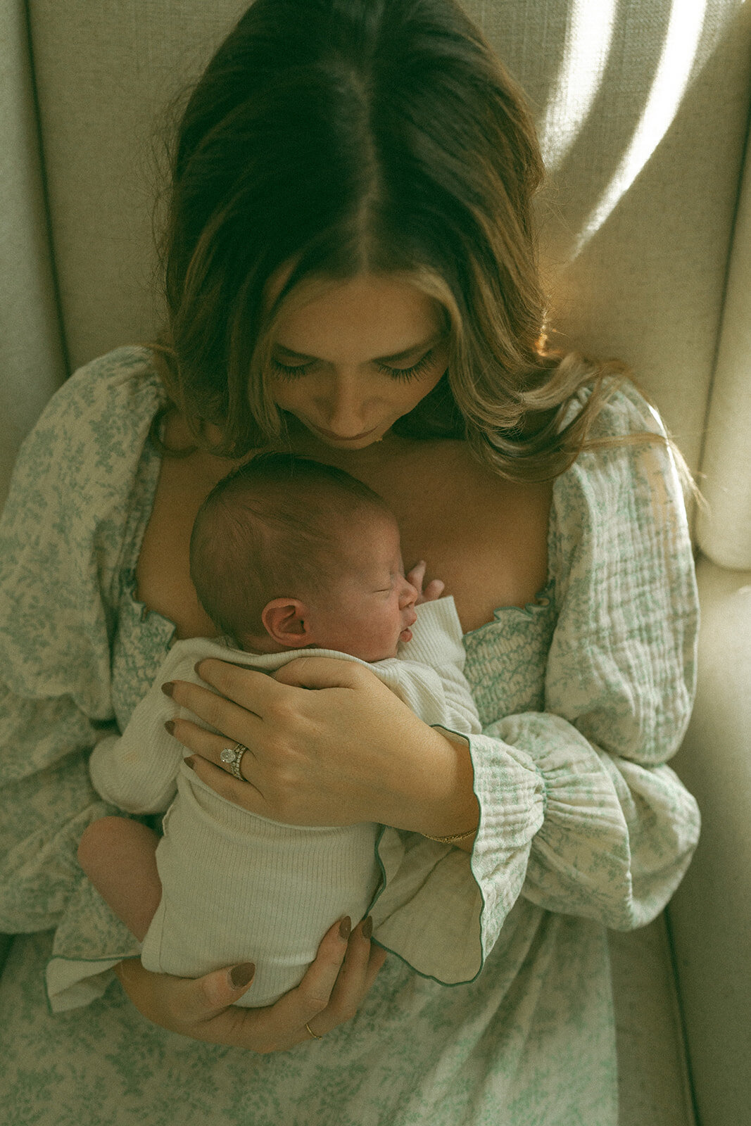 Mother sitting in a rocking chair with her newborn baby resting on her chest during an intimate lifestyle session
