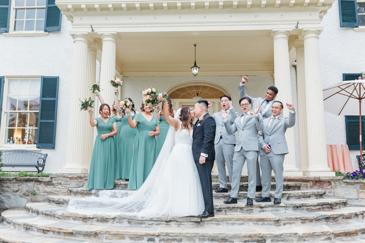 Bride and groom kissing with wedding parties in the back