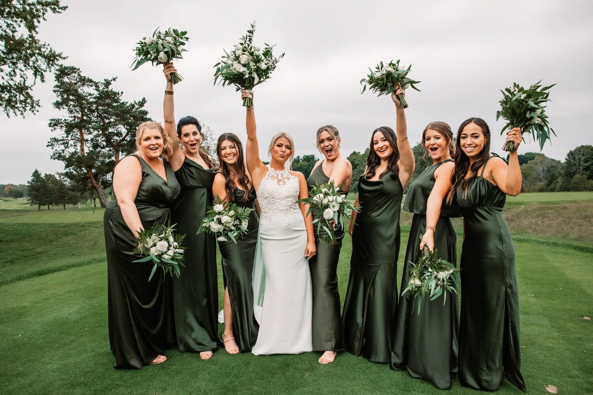 bride and bridemaids cheer and hold flowers on golf course