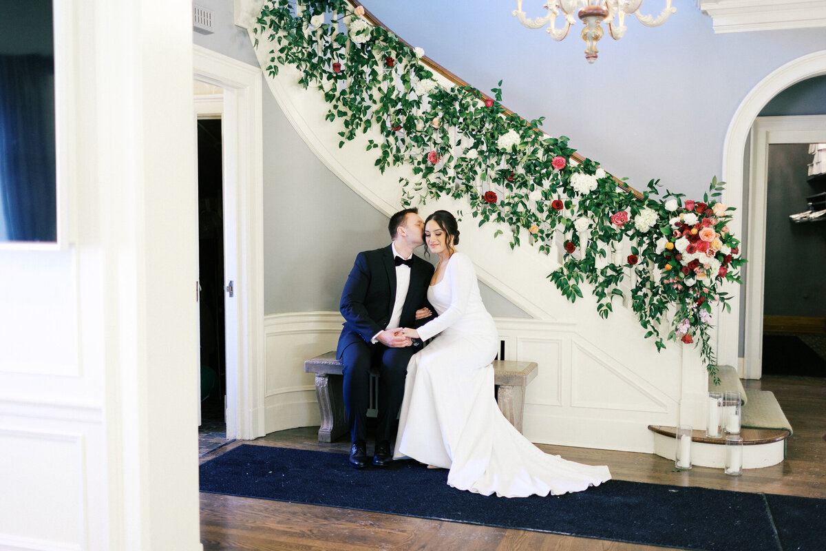 While sitting down on the bench at St. Paul College Club, the groom is kissing his bride.