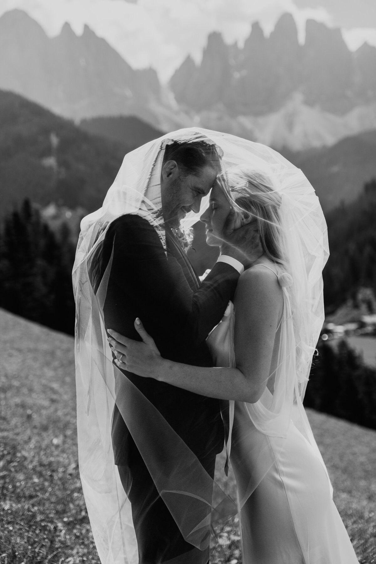 Romantic couple kiss under veil with mountain backdrop