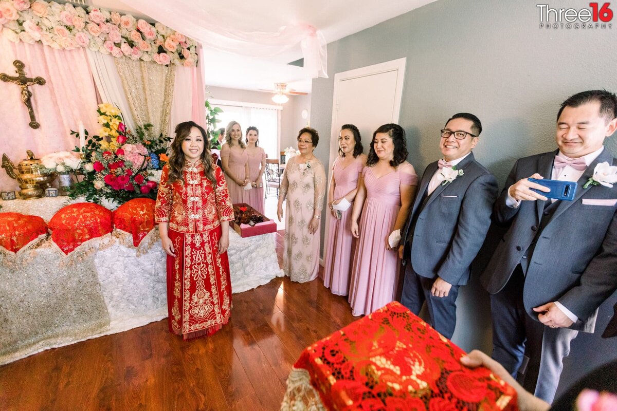 Bride poses in her red dress as bridal party and her mother look on