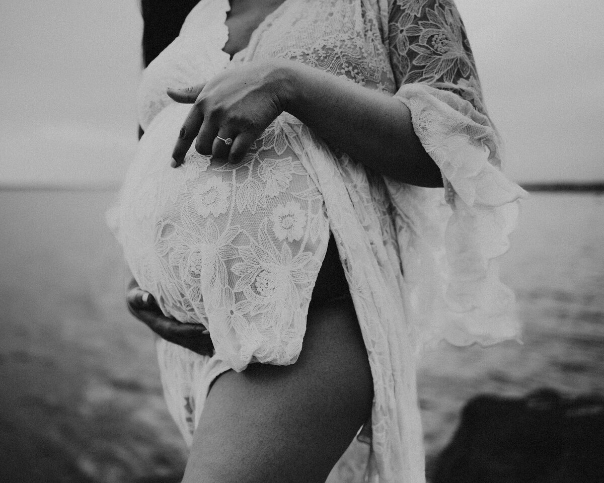 Photo of a woman's pregnant belly in front of the sea, wearing a white dress