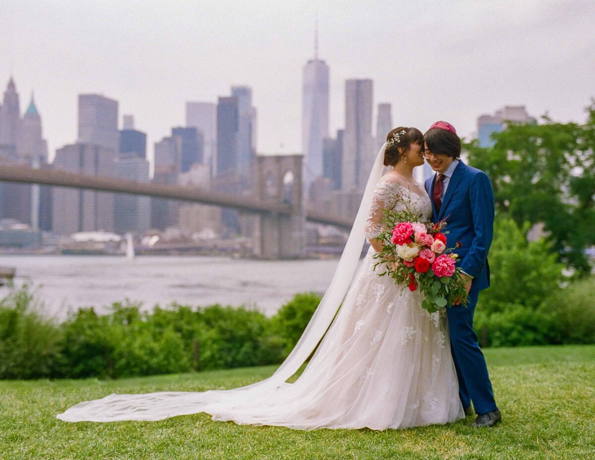 A couple standing in a small park overlooking a city skyline.