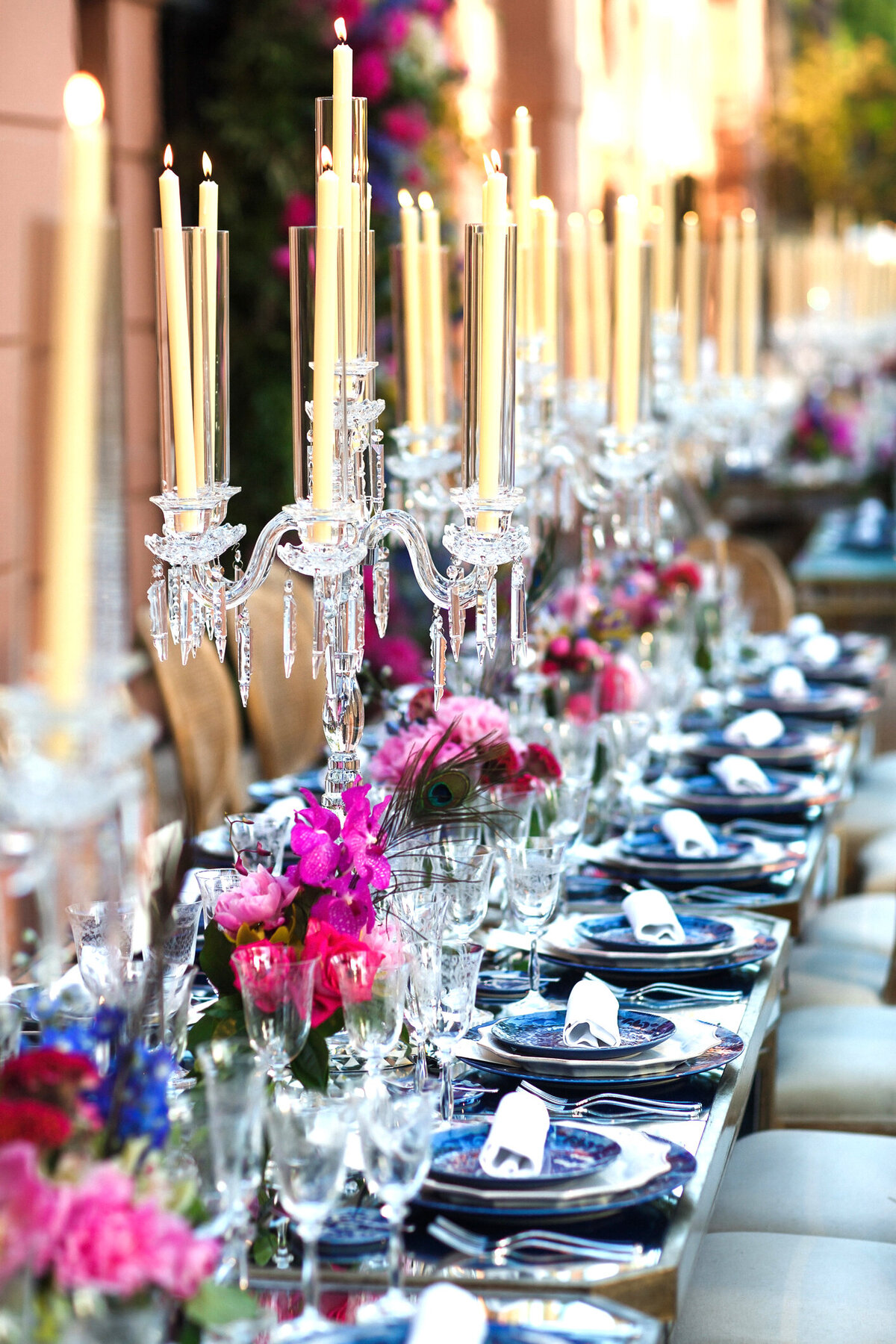 A sophisticated wedding tablescape featuring elegant blue china, lush pink florals, and exquisite glass candelabras. The blend of timeless tableware, romantic blooms, and soft candlelight creates a refined and luxurious reception setting, perfect for couples seeking an elevated wedding aesthetic.