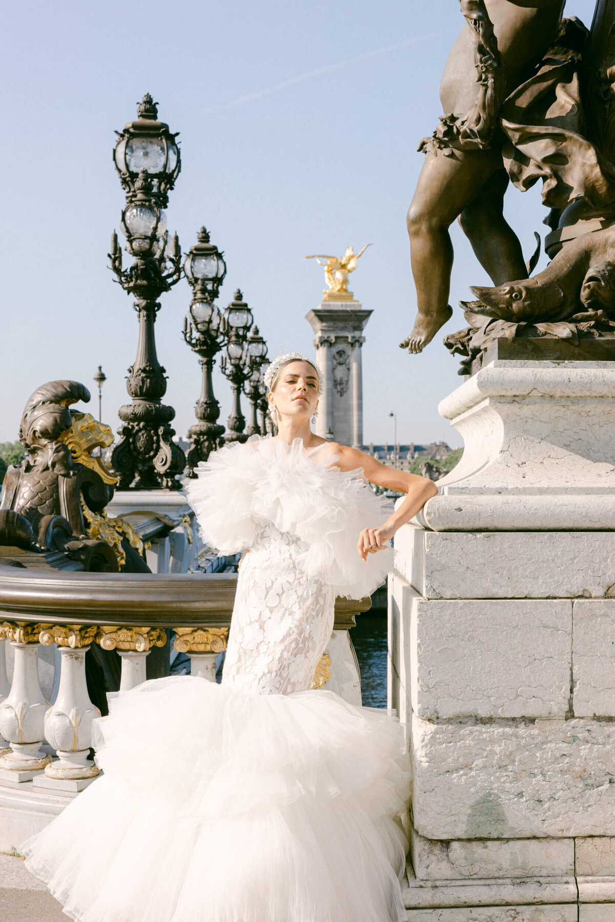 a picture of a bride in a elaborate puffy white wedding dress she is posing on the Pont Alexandre III bridge in Paris France