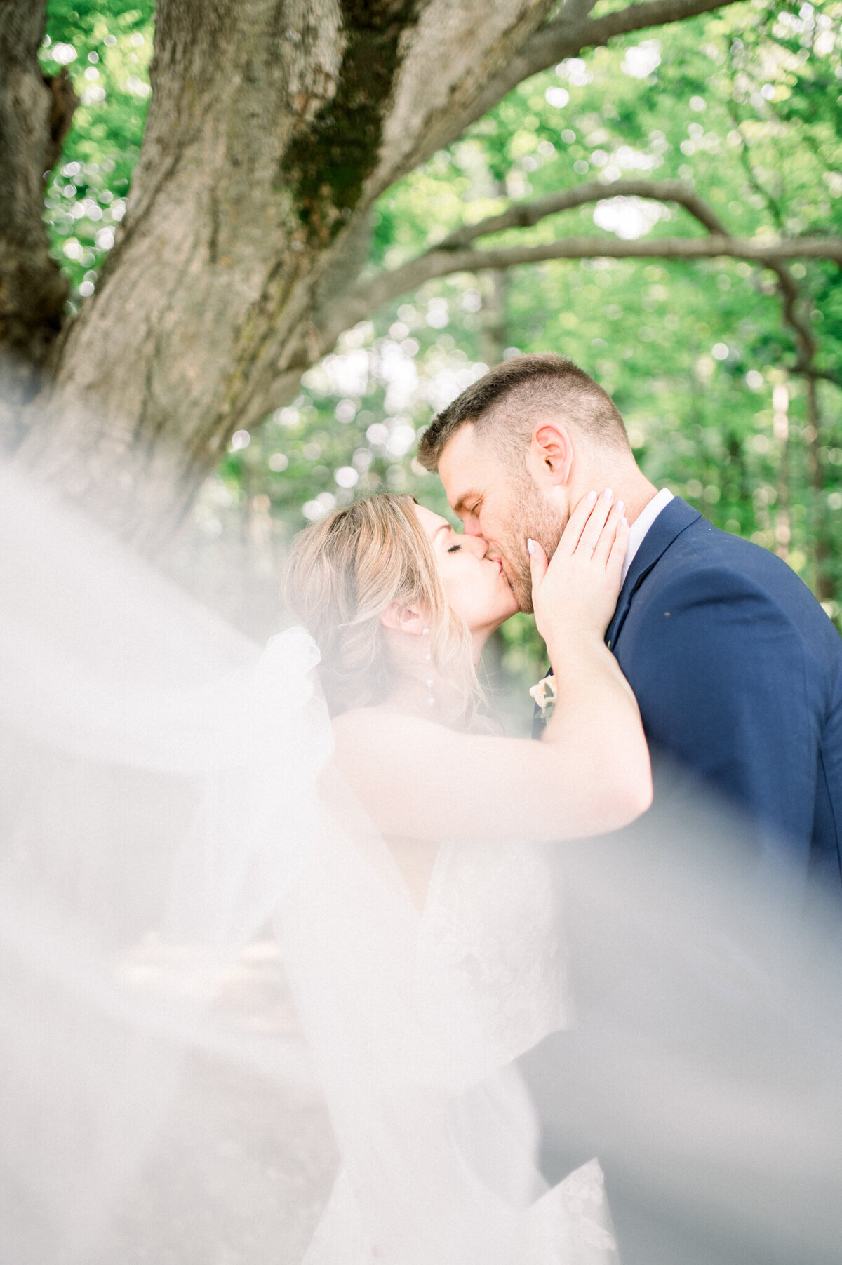 Bride and groom kissing with veil blowing in front of the camera captured by Niagara wedding photographer