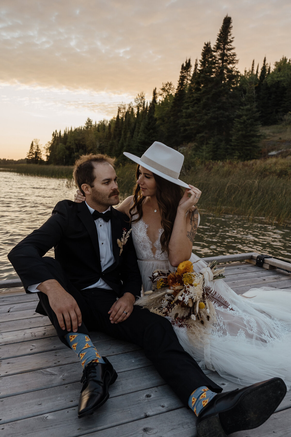 bride and groom sitting on dock by lake