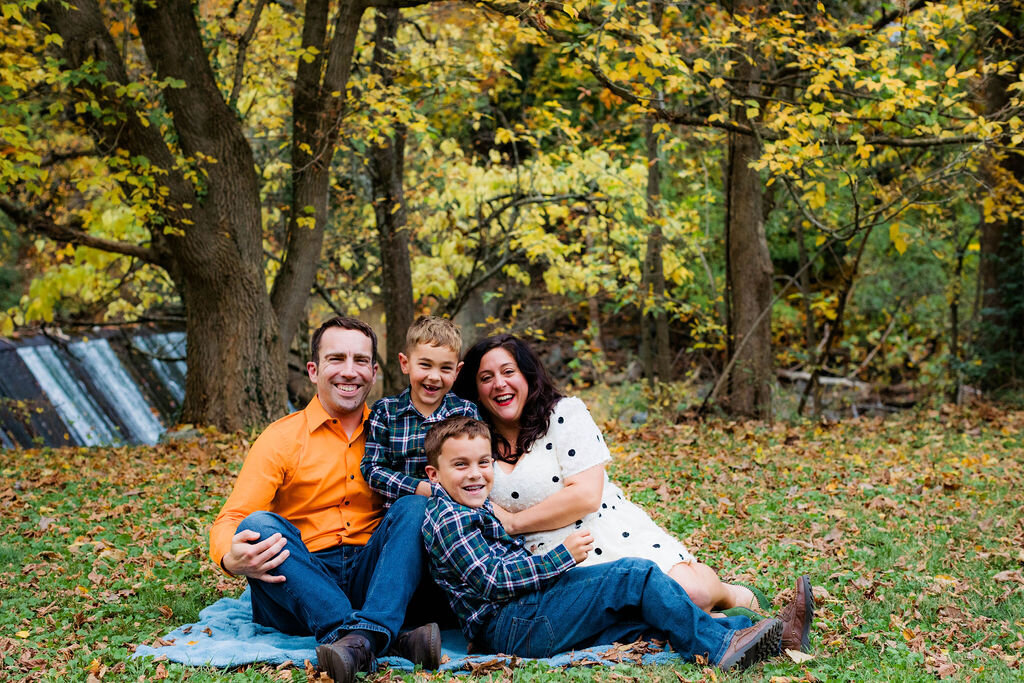 A family of four smiles on a picnic blanket.