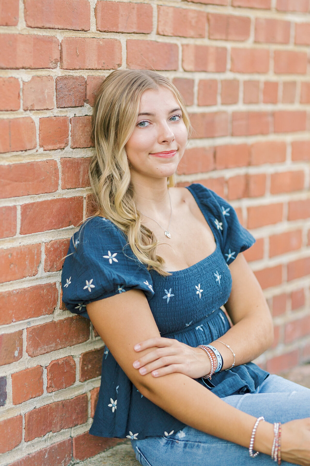 A high school senior leaning against a brick wall in downtown Raleigh, smiling softly — Raleigh portrait photographer.
