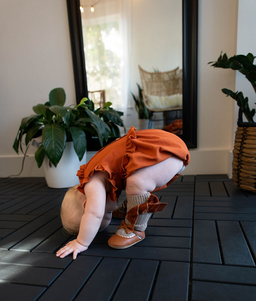 A one year old bent over with their feet and head on the ground.