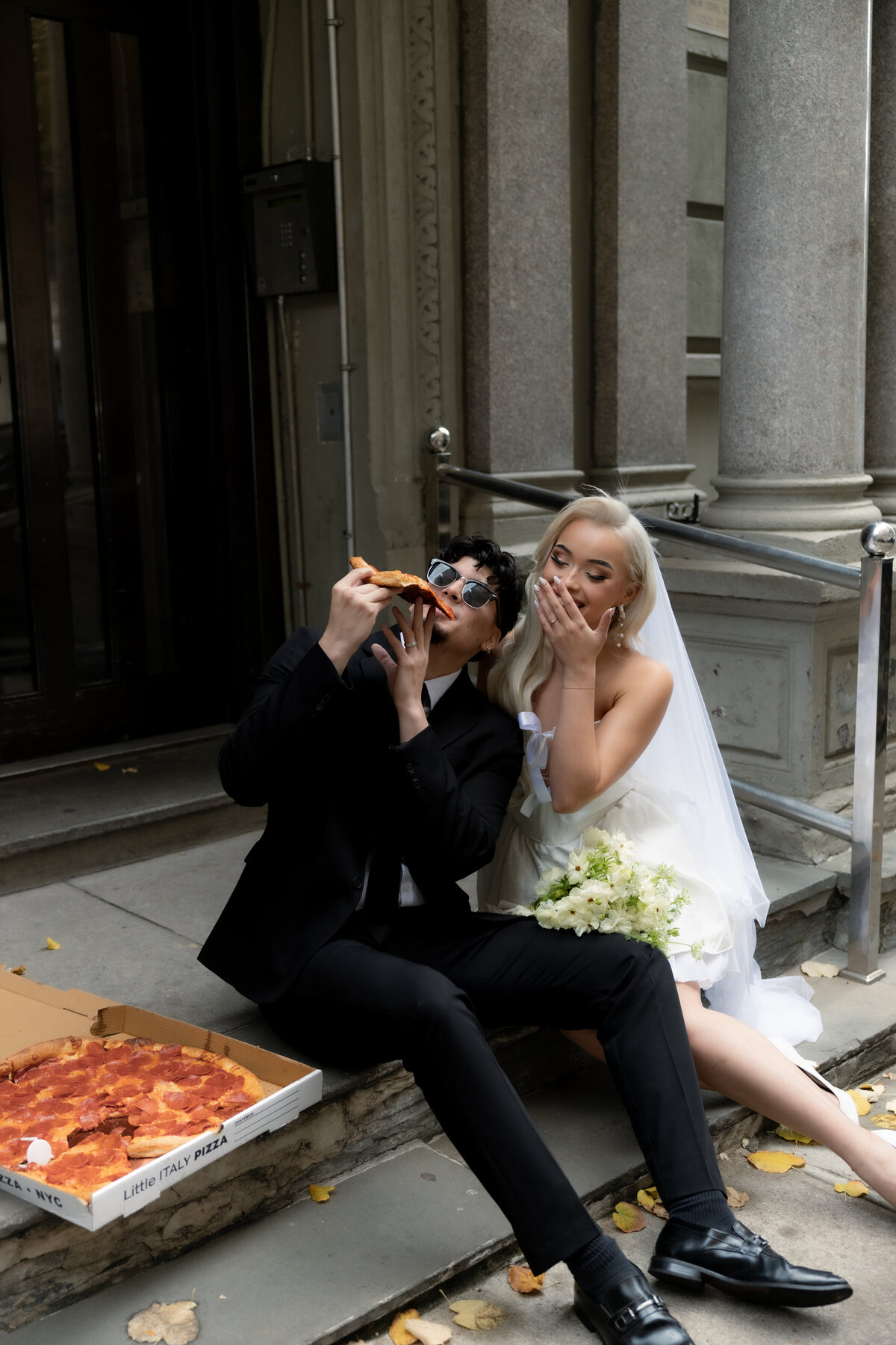 A creative shot of the pizza box open on a street corner in NYC, with the couple laughing in the distance.