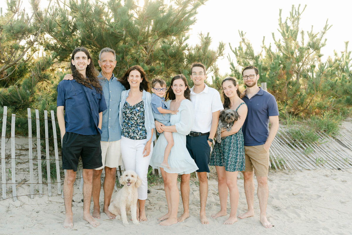 extended family dressed in blue and white poses with two dogs at sunset