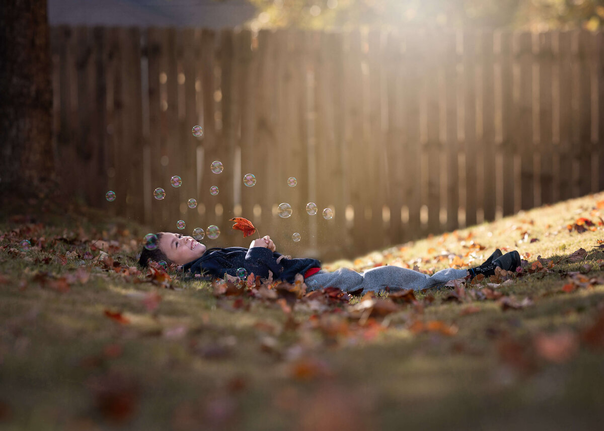 playful boy  laying on the floor holding a fall leaf while seign bubbles falling at him