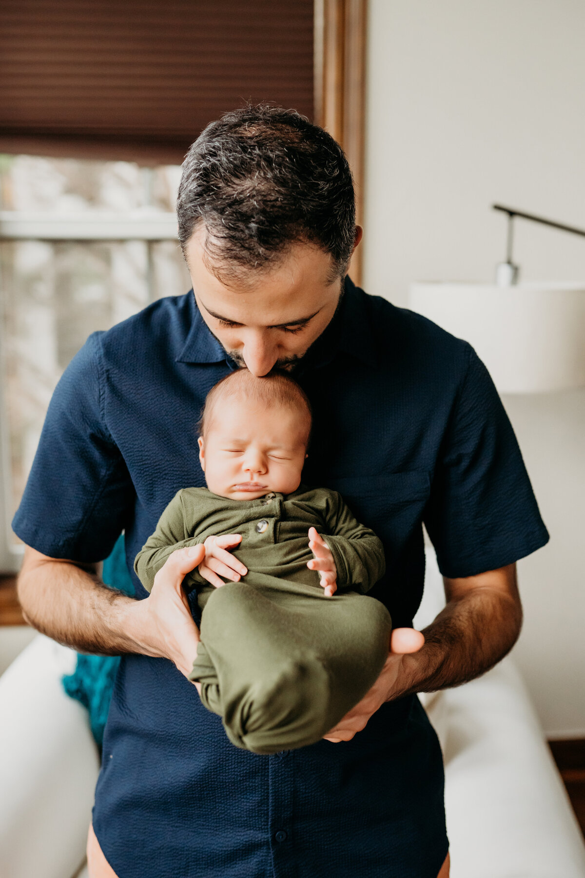 Newborn photographer, a father holds his newborn baby son and kisses him on the head