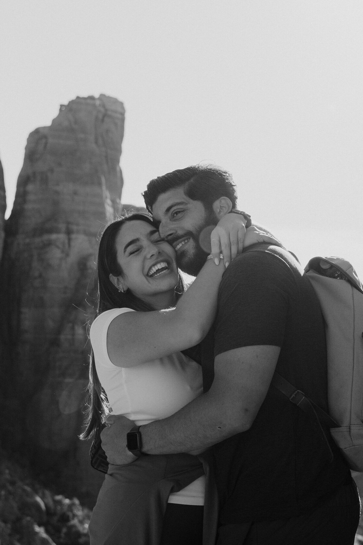 Couple hugging and smiling after hiking to the top of Cathedral Rock in Sedona, Arizona for surprise proposal.