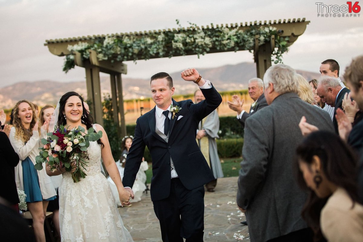 Bride and Groom cheer as they walk down the aisle between their guests