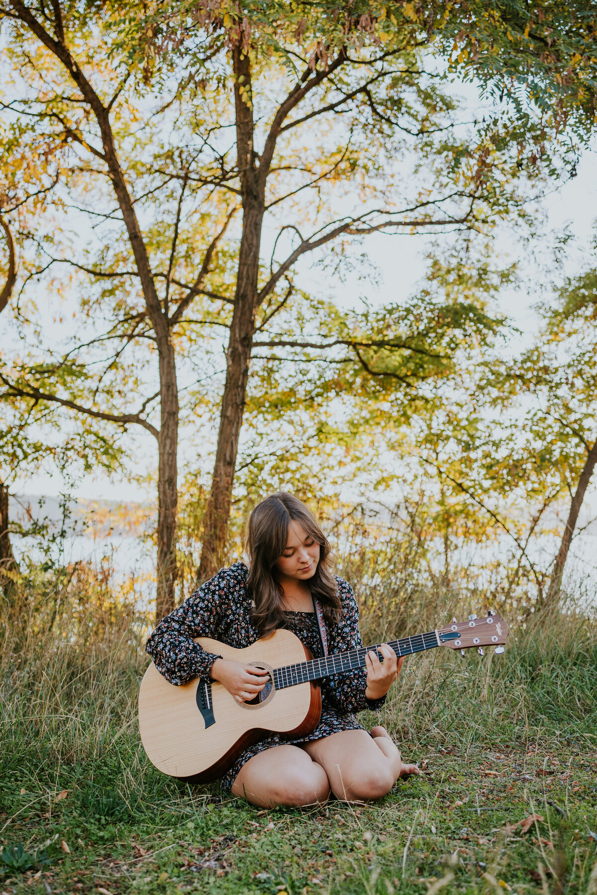 Young woman sits in grass while playing guitar.
