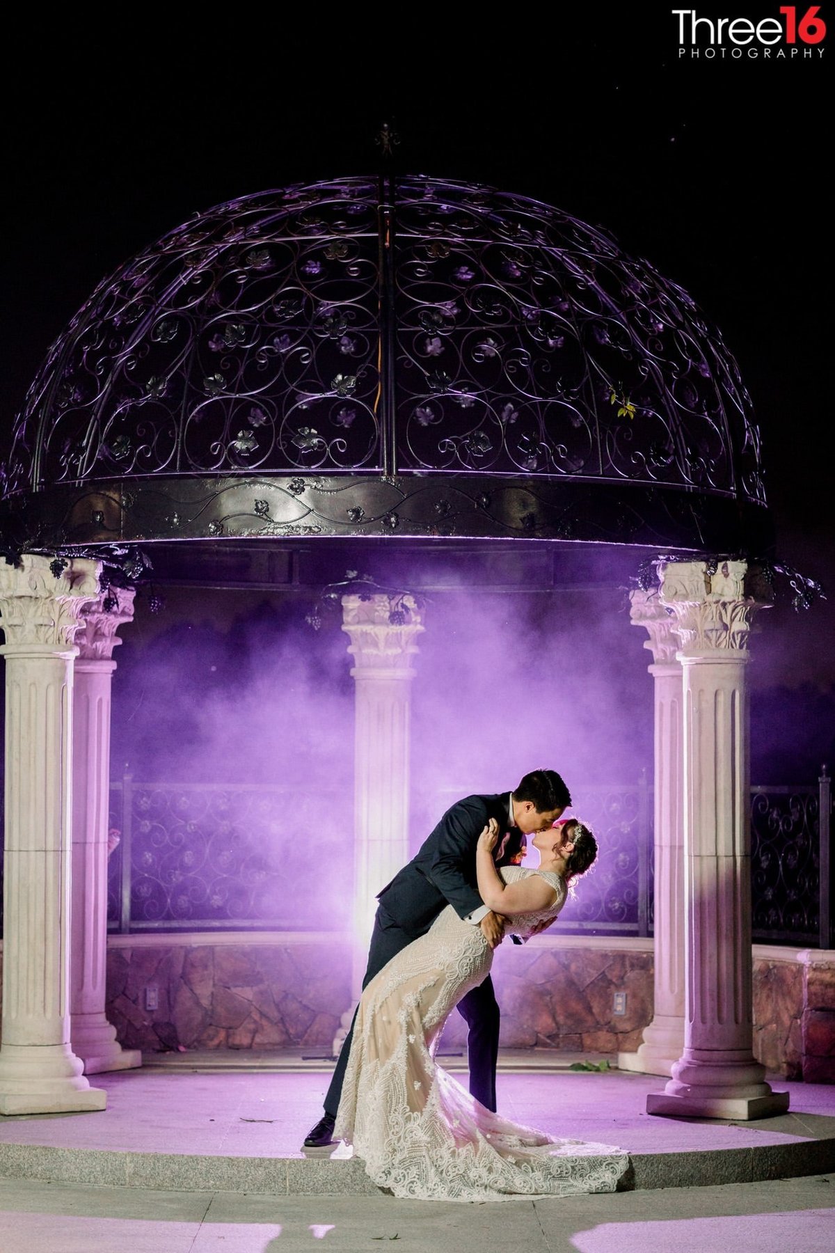 Groom dips his Bride and kisses her under the purple haze gazebo
