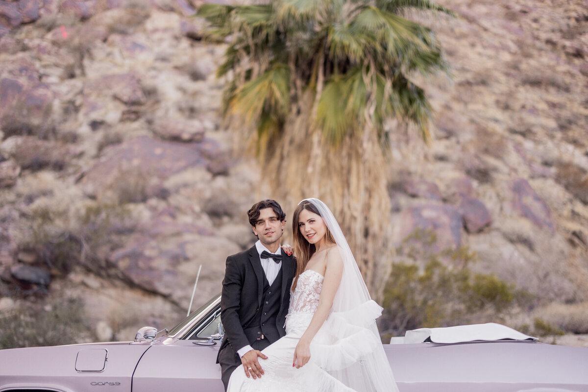 Couple walking together in desert terrain, dressed in formalwear with a rocky backdrop and soft natural light.