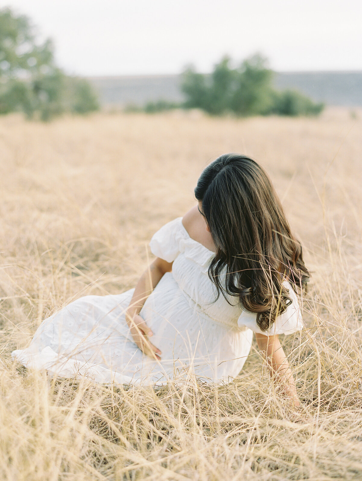 Pregnant woman in a long white dress sitting in a grassy field