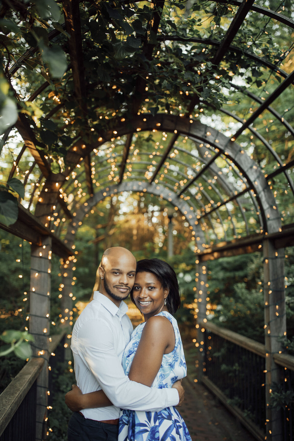 Black couple posing under twinkle lights during spring engagement shoot at Sayen House and Gardens in Hamilton Township New Jersey
