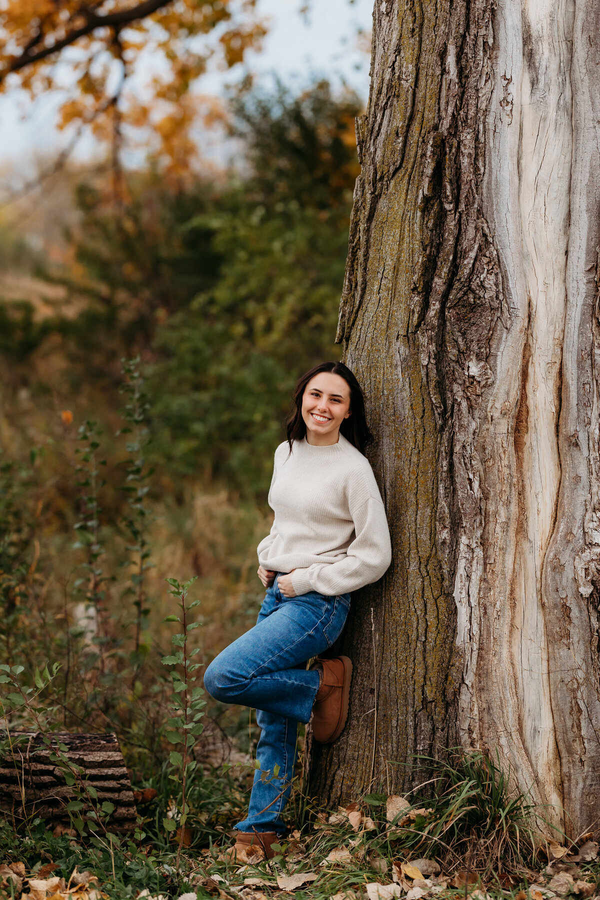 A girl leans on a tree with a foot up.