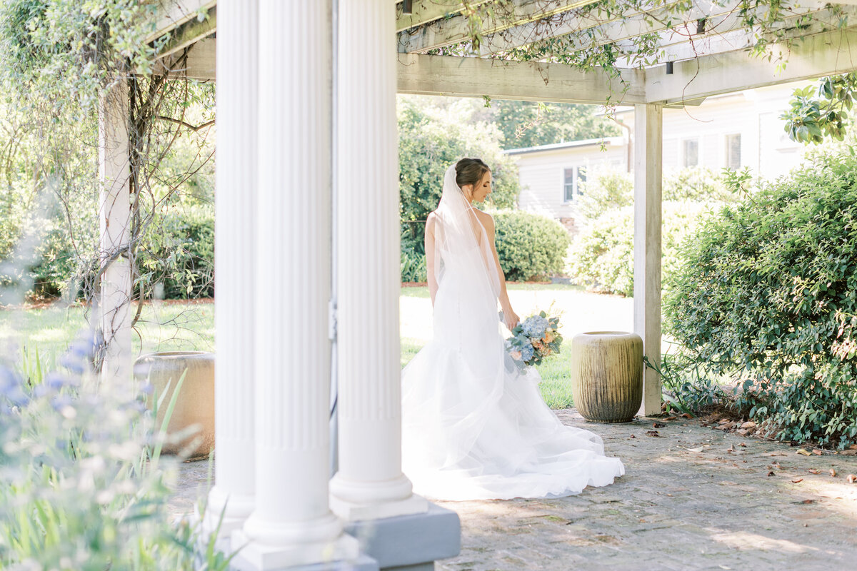 A bride looks over her shoulder while standing under a trellis.