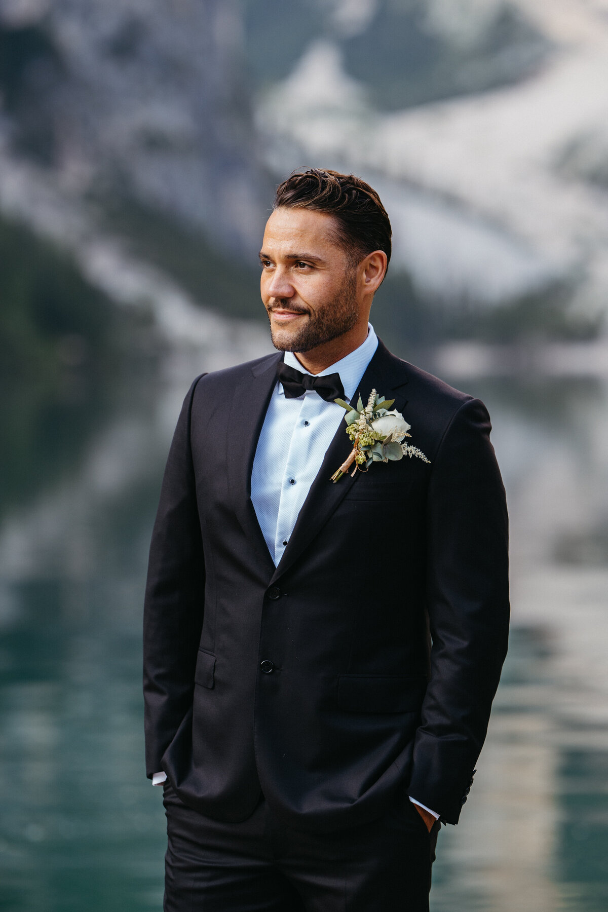 Groom smiling in tuxedo by the lake in the Dolomites