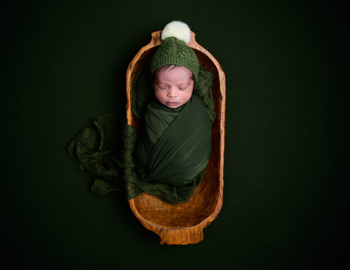 A tiny newborn baby is sleeping in a long bowl during his newborn photo session in Bremerton. Image photographed by E. Benecki Photography.