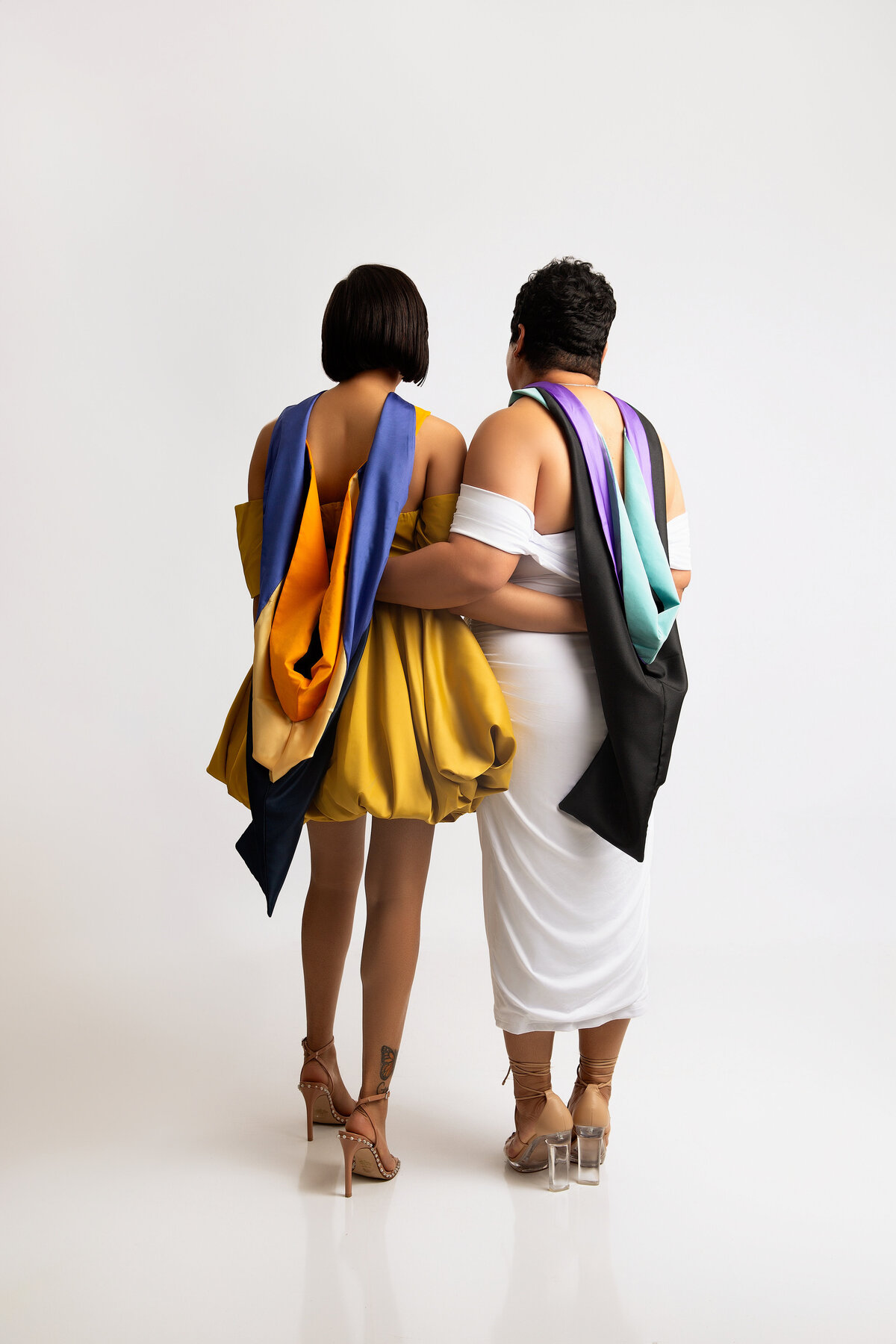Mother and daughter posing side by side with their masters cape for graduation portrait.