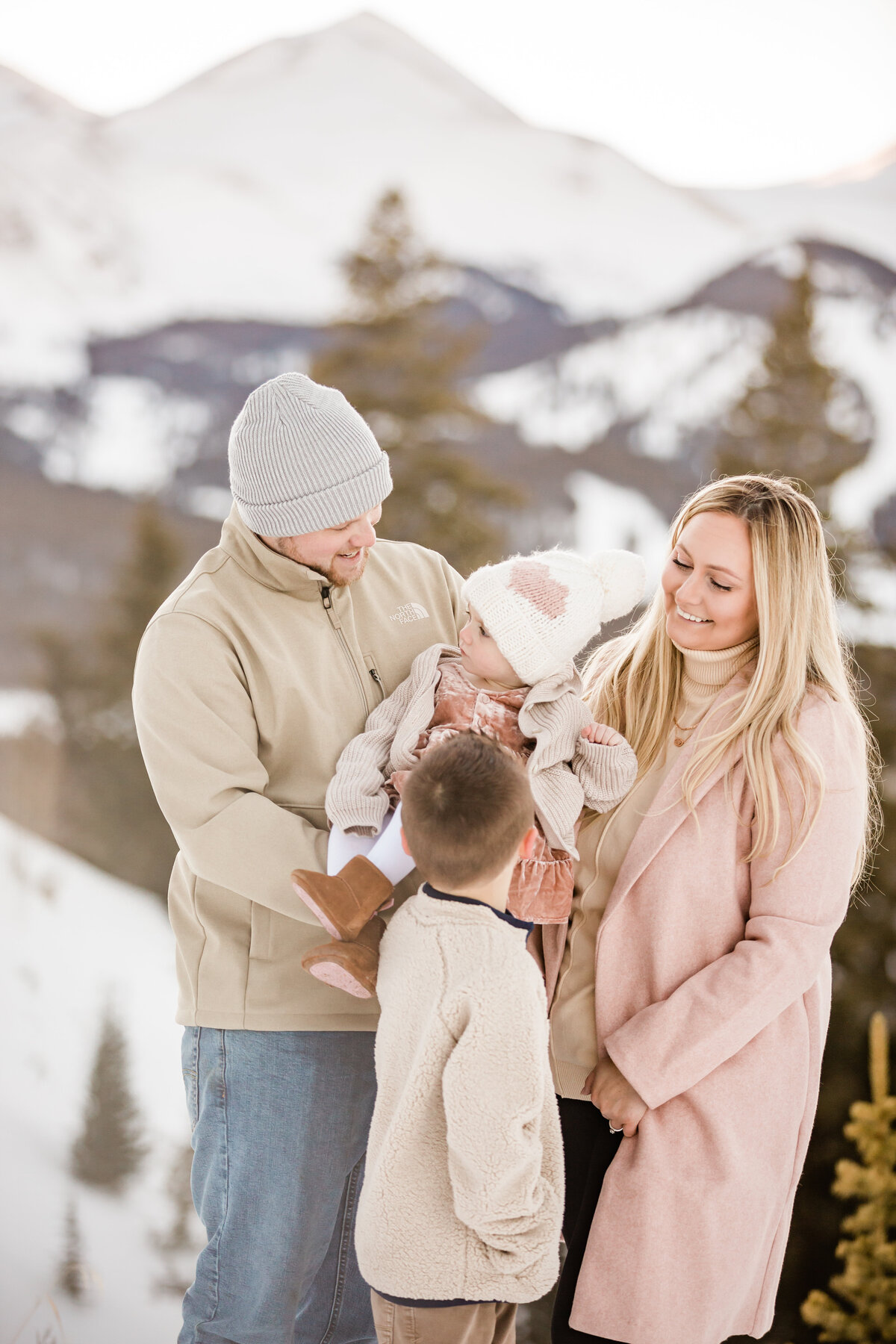 Mom, Dad, and their young children are huddled together and smiling on a winter day with their Breckenridge Family Photographer